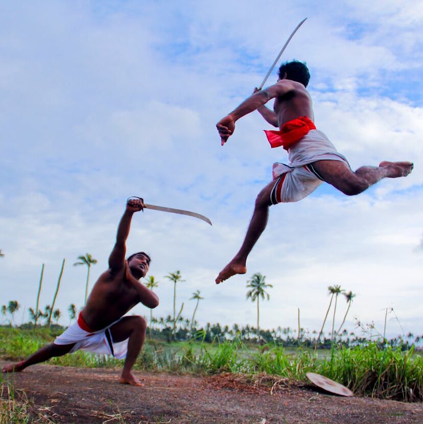 Two Kalaripayattu practitioners in dynamic combat inside a traditional kalari